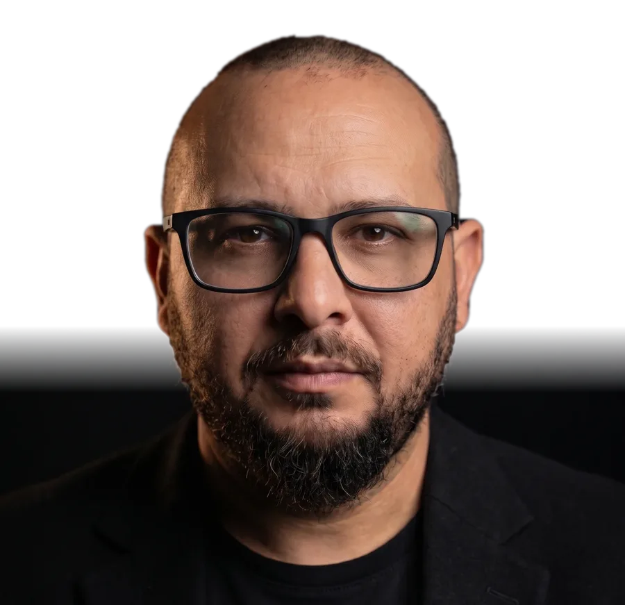 Henrique Plácido, de óculos e blazer preto, olhando para a câmera