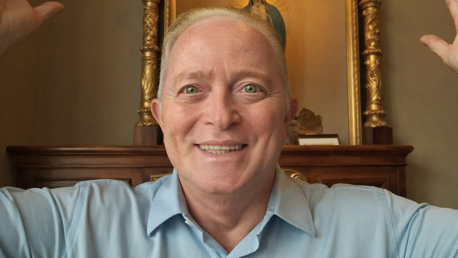Retrato de um homem sorrindo em uma sala com moldura dourada ao fundo